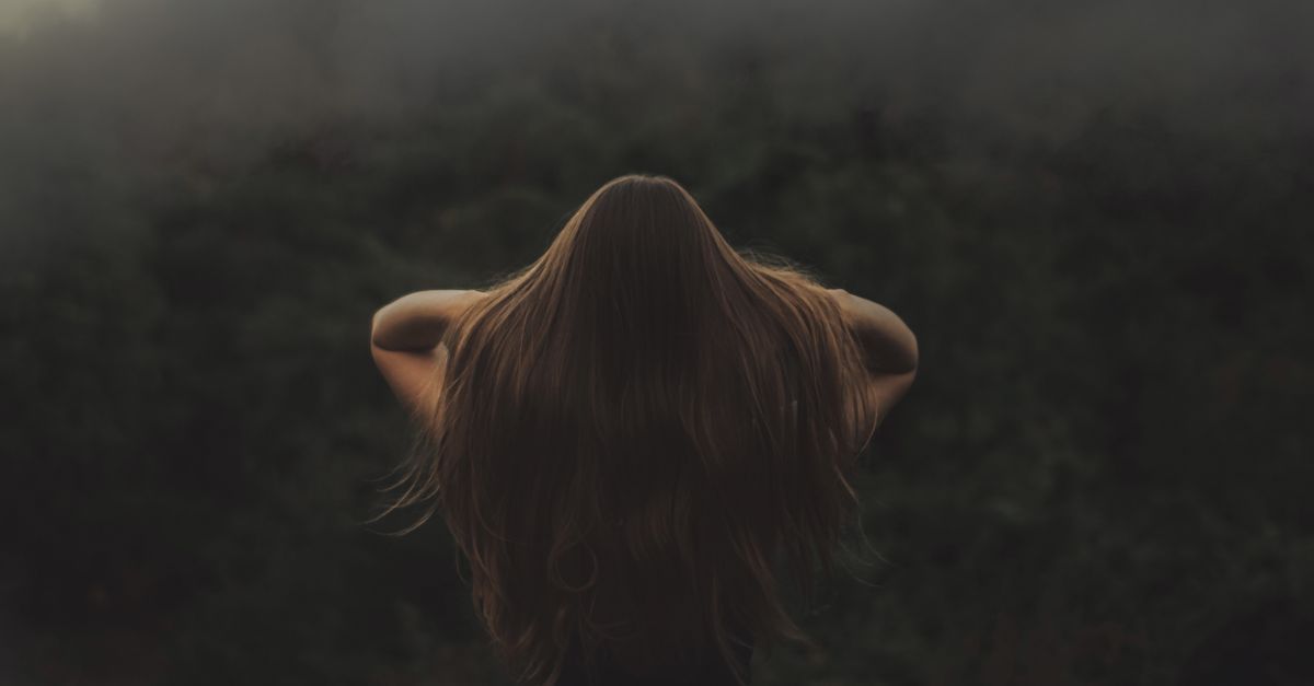 Back view of a woman with long hair, standing in a misty forest.